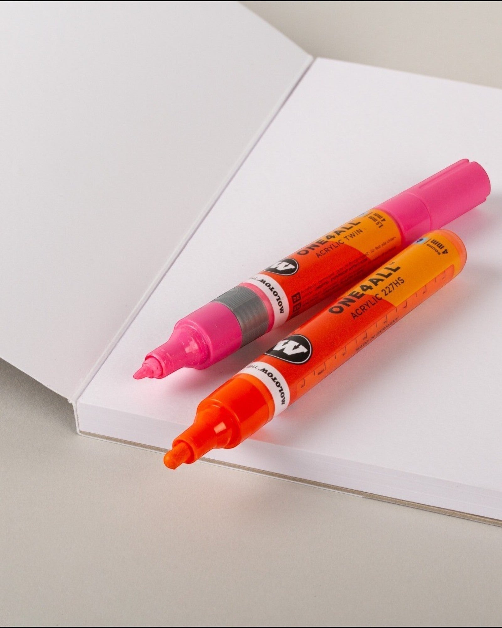 Astrofat A4 sketchbook with pink and orange Molotow acrylic markers resting on open white paper pages.