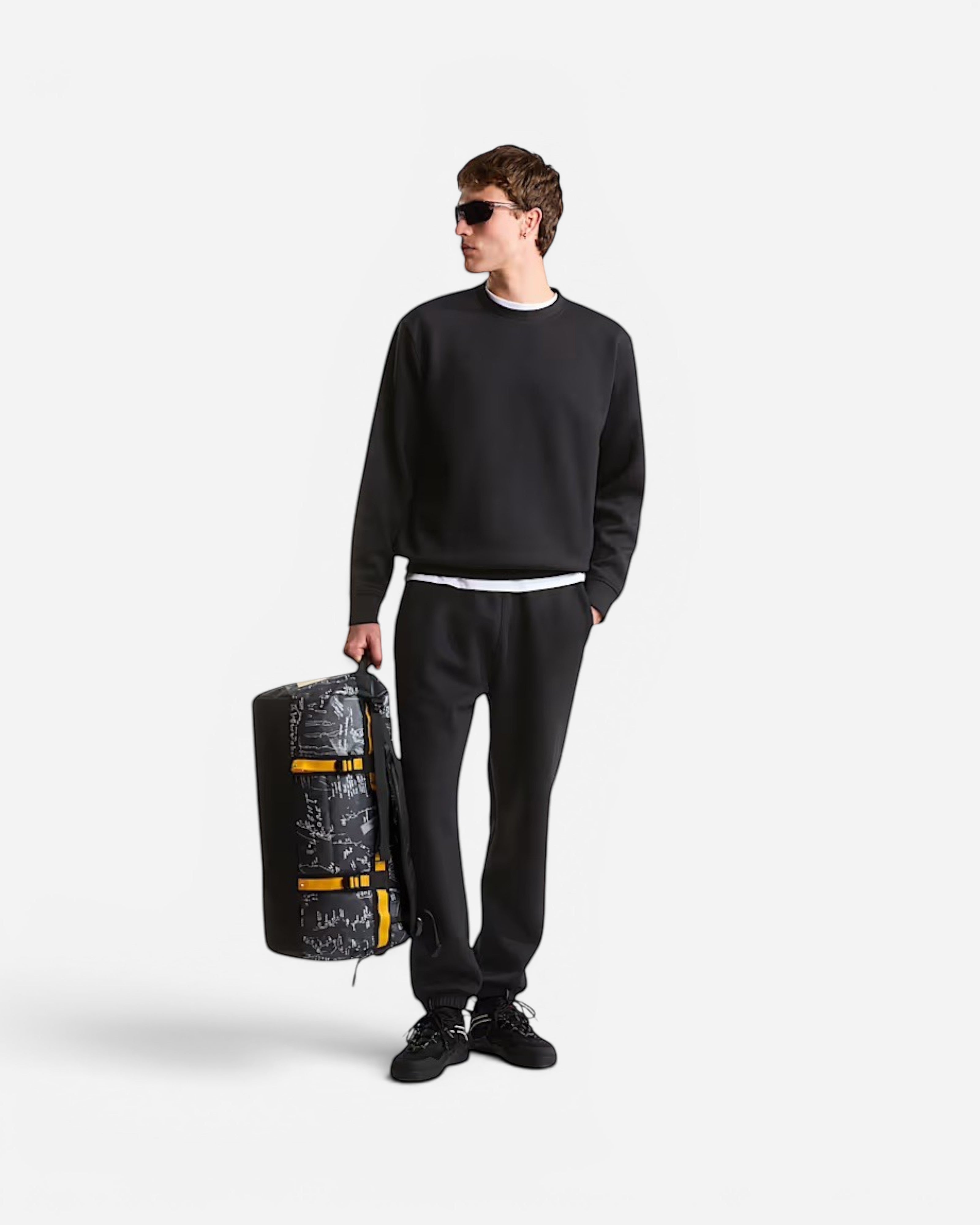 Astrofat model holding a 50L Base Camp Duffel in anthracite grey with a topographic print and bright yellow accents.