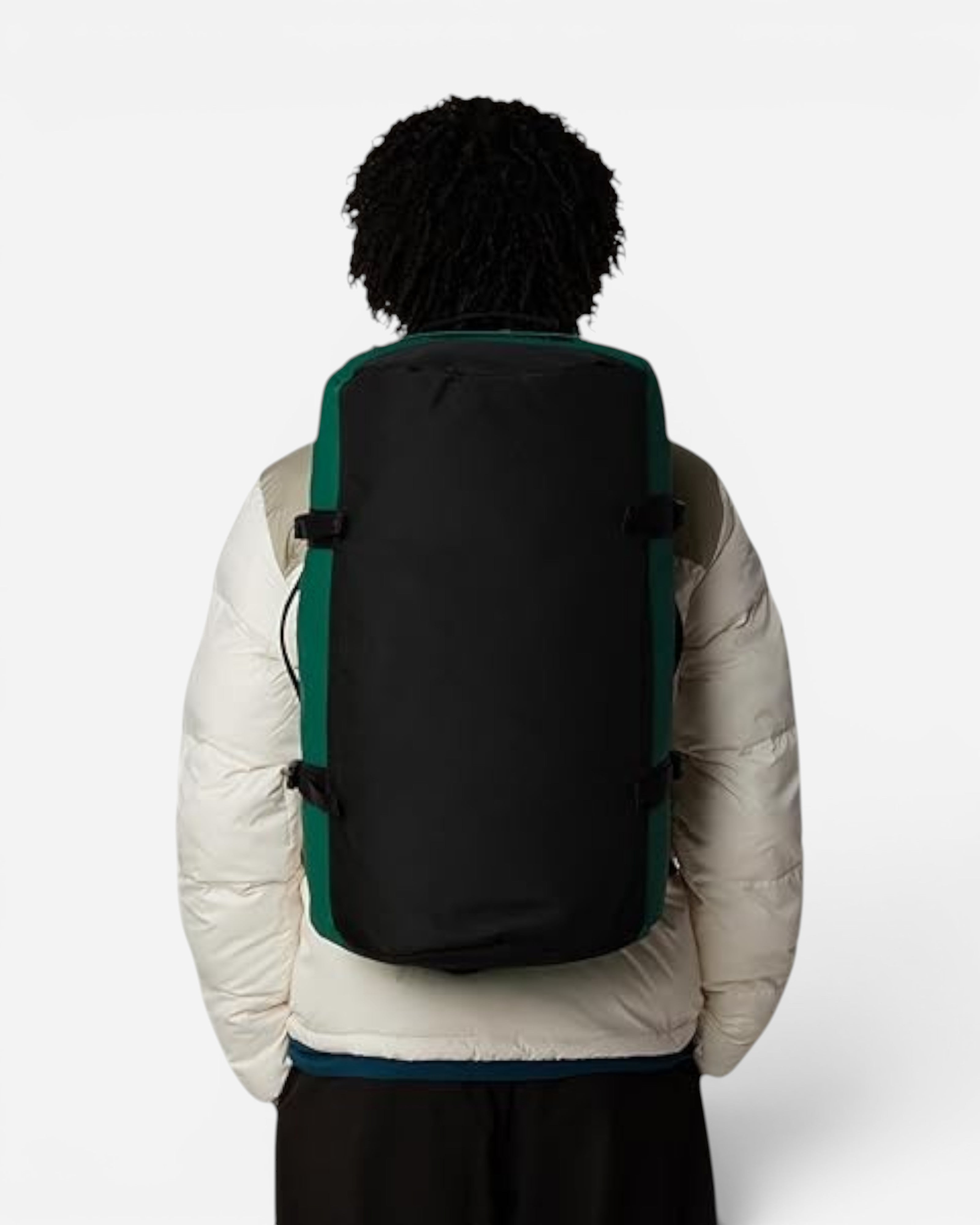 Astrofat Base Camp 50L duffel bag in evergreen and black worn as a backpack by a person in a white puffer jacket.