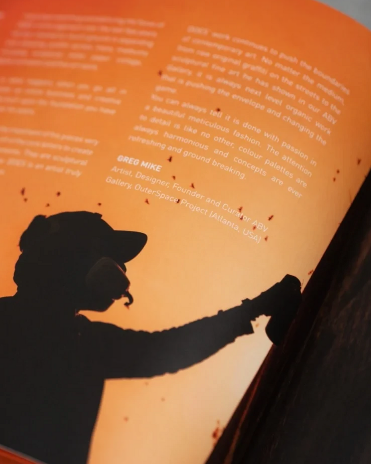 Astrofat DOES First 20 Years book featuring an orange page with a silhouette of an artist using a spray can