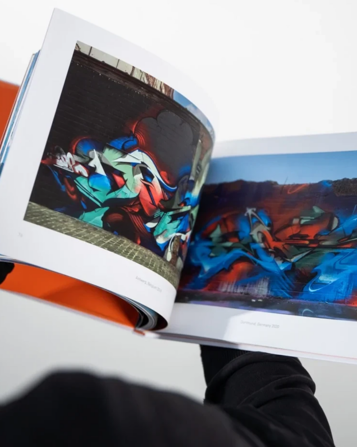 Astrofat DOES First 20 Years book open, showing colorful graffiti mural photos on glossy pages with orange cover