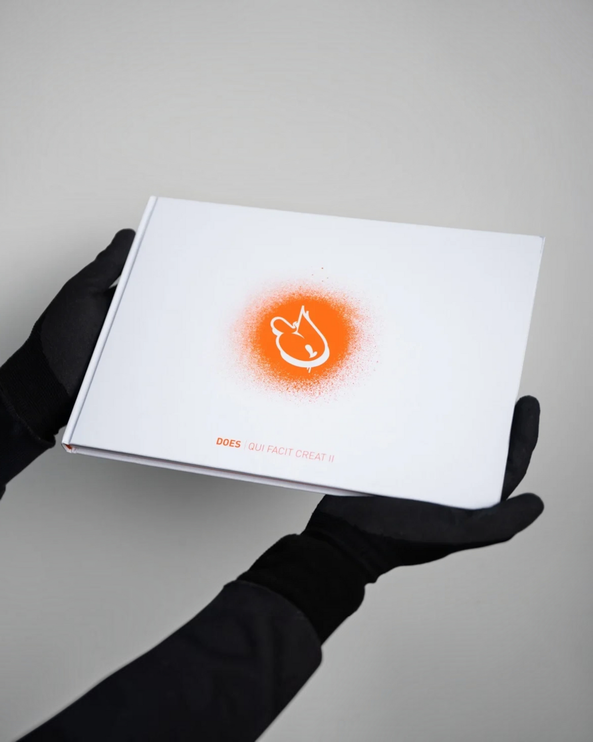Astrofat DOES First 20 Years hardcover book with orange spray paint graphic held by hands in black gloves.