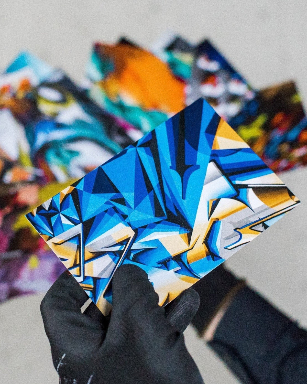 Astrofat DOES Pieces Postcard Set N°3 featuring vibrant blue graffiti art held by a hand in a black glove.