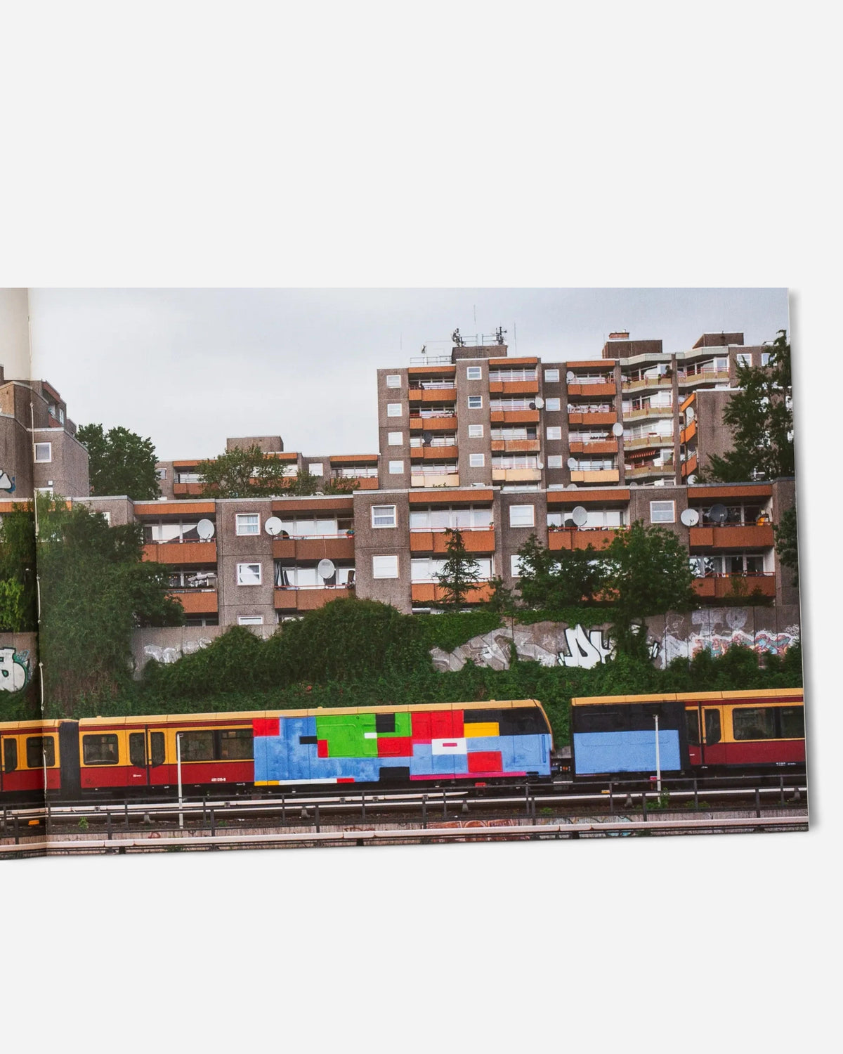 Astrofat Farbzüge book page showing a graffiti-covered Berlin train passing by a concrete residential building.