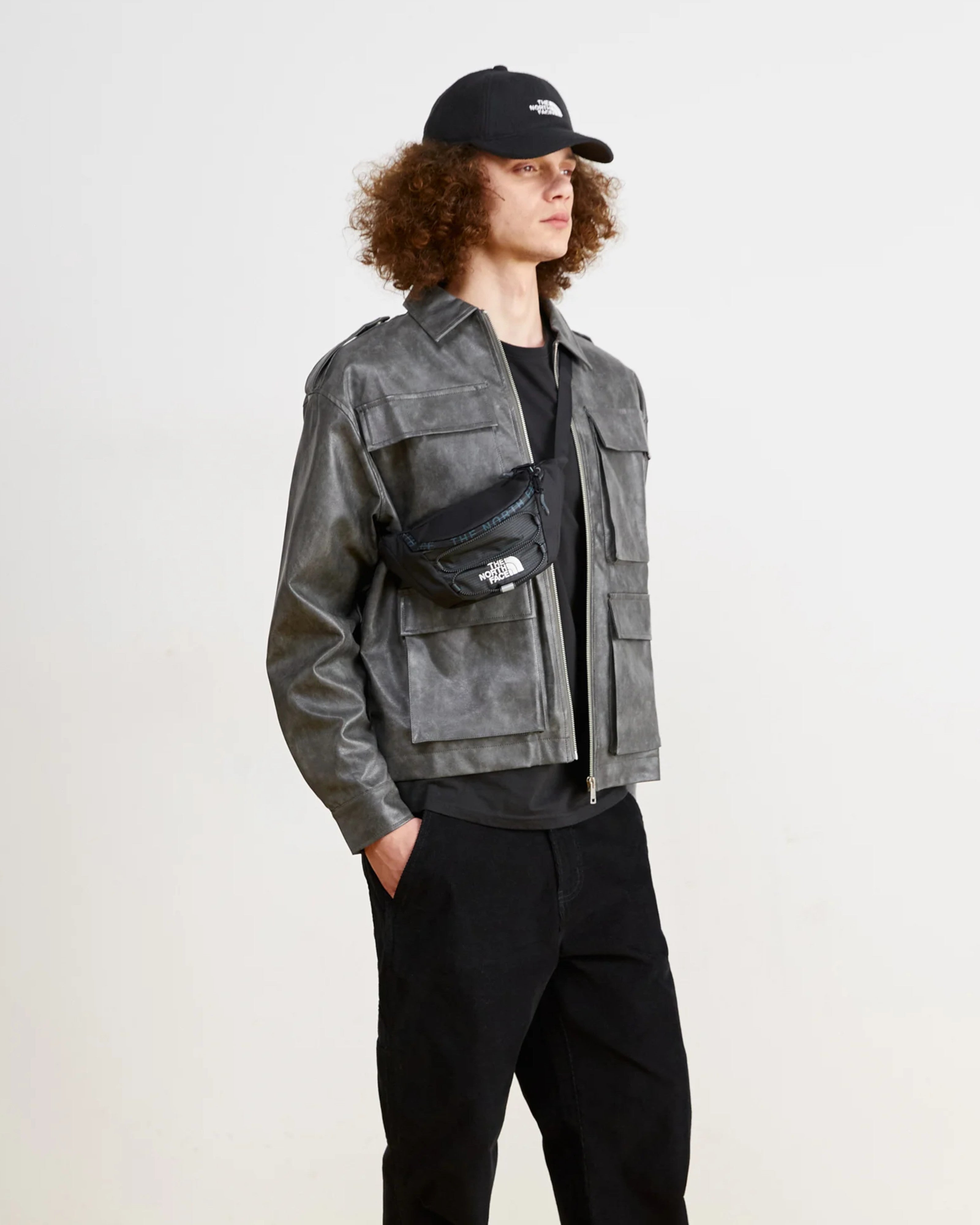 Astrofat Jester Lumbar bag in asphalt grey and TNF black, worn by a male model with a grey jacket and black cap.