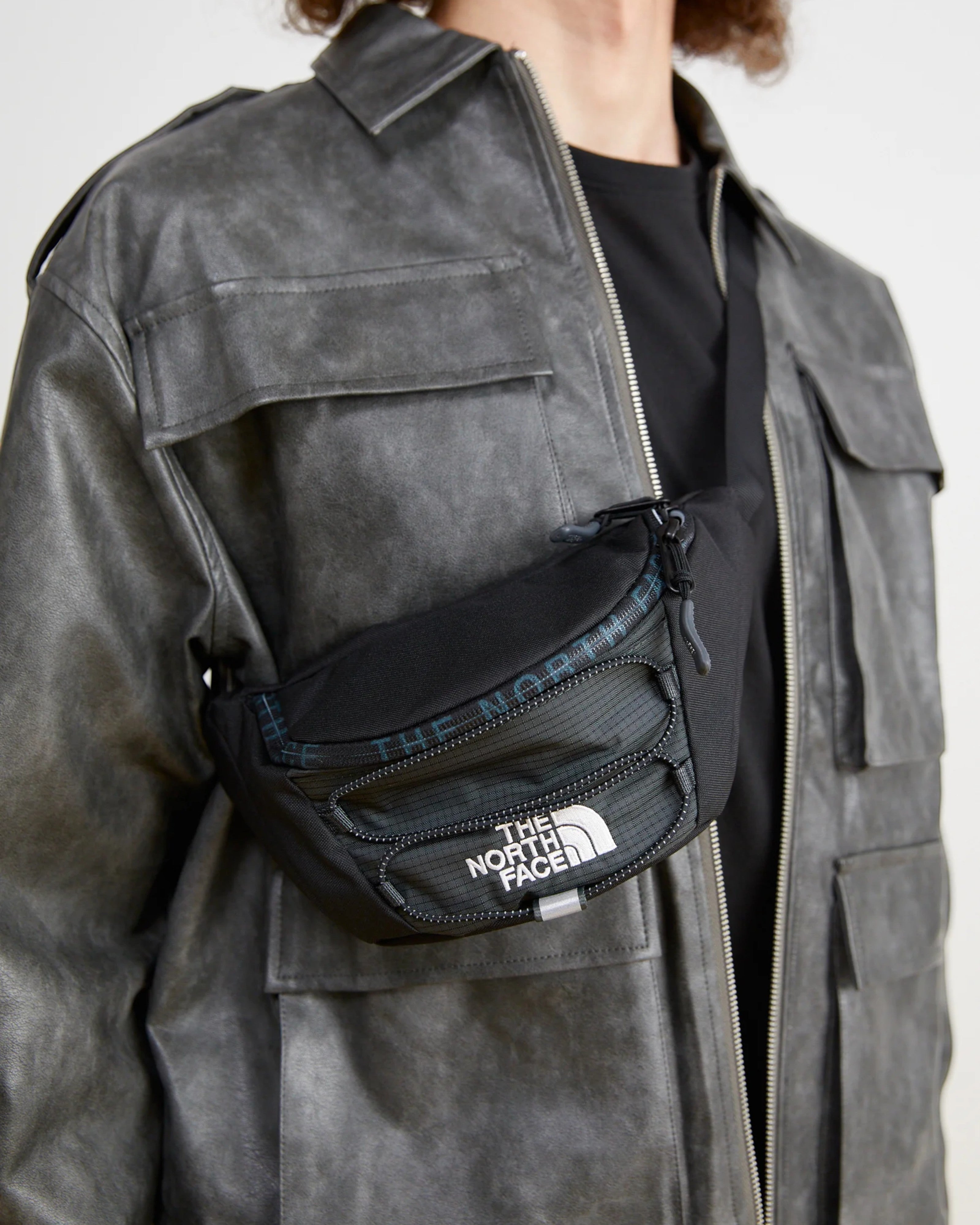 Astrofat Jester Lumbar bag in asphalt grey and TNF black, made of durable Base Camp material, worn crossbody by a model.