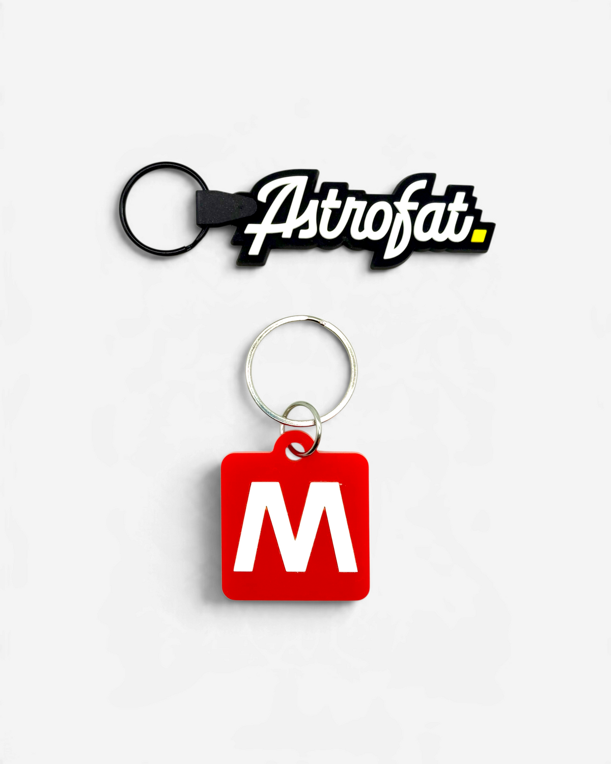 Astrofat Milano keychain set featuring a black rubber logo tag and a red square tag with a white letter M