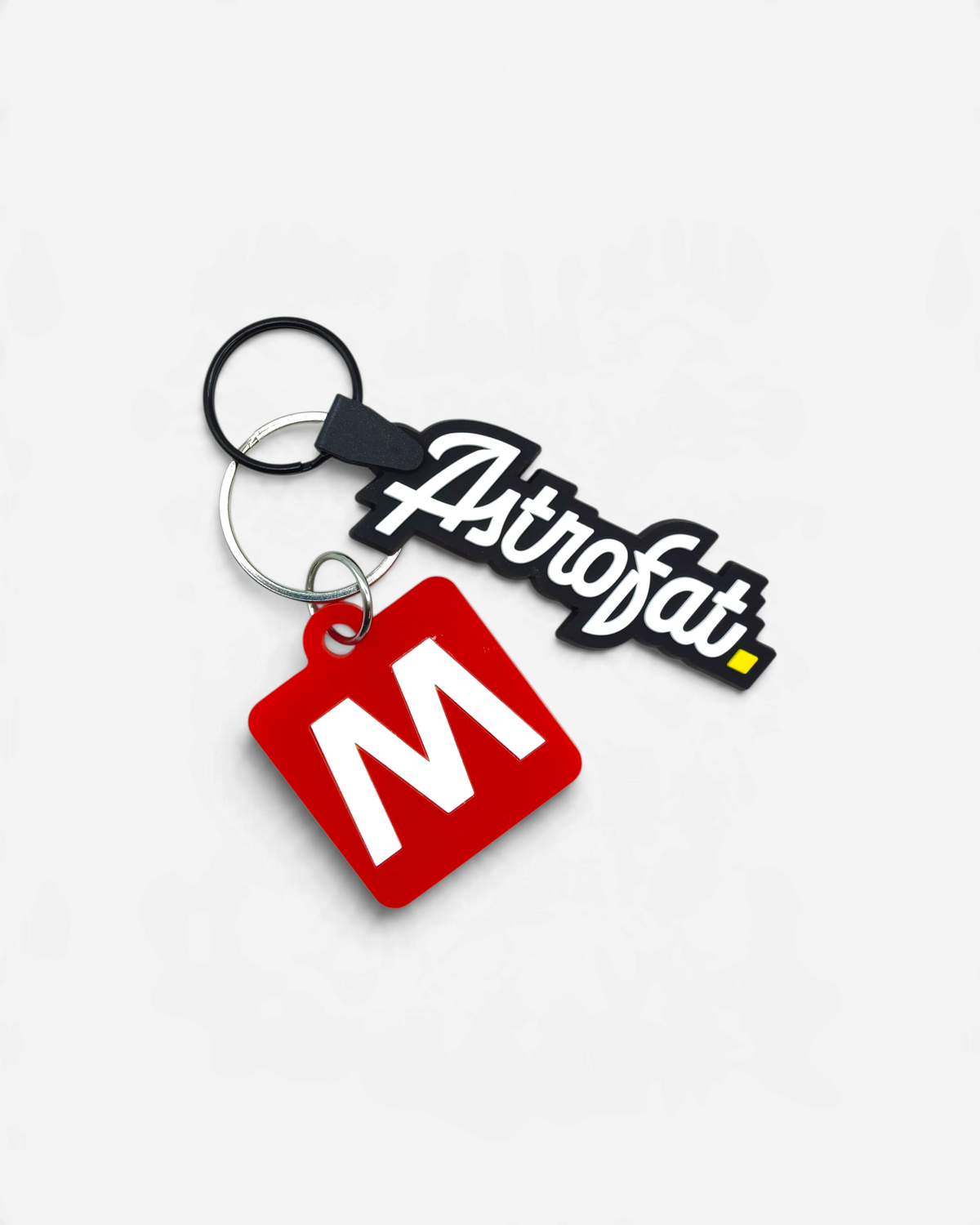 Astrofat Milano keychain set featuring a black rubber brand logo tag and a square red acrylic tag with a white M