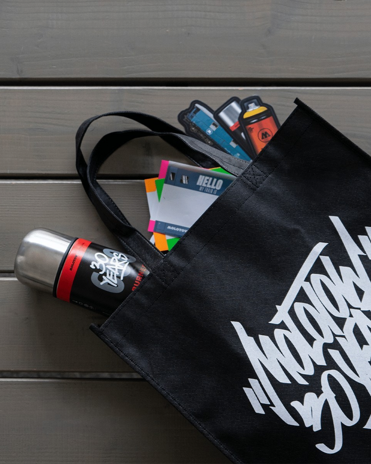 Astrofat black cotton spray can bag with Molotow logo, holding spray paint cans and stickers on a wooden surface.