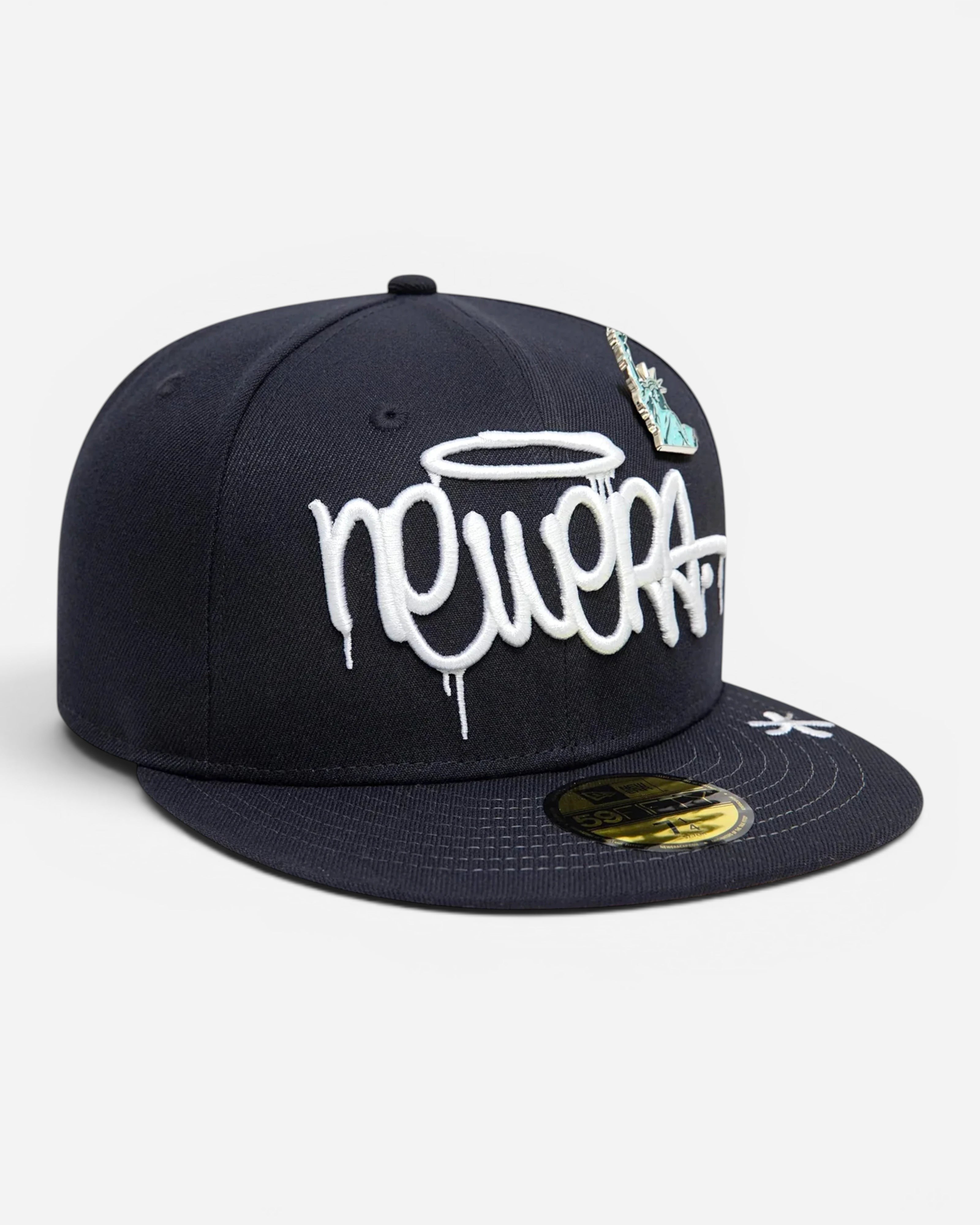Astrofat 59FIFTY New Era navy blue fitted cap with white graffiti-style embroidery and a Statue of Liberty pin.