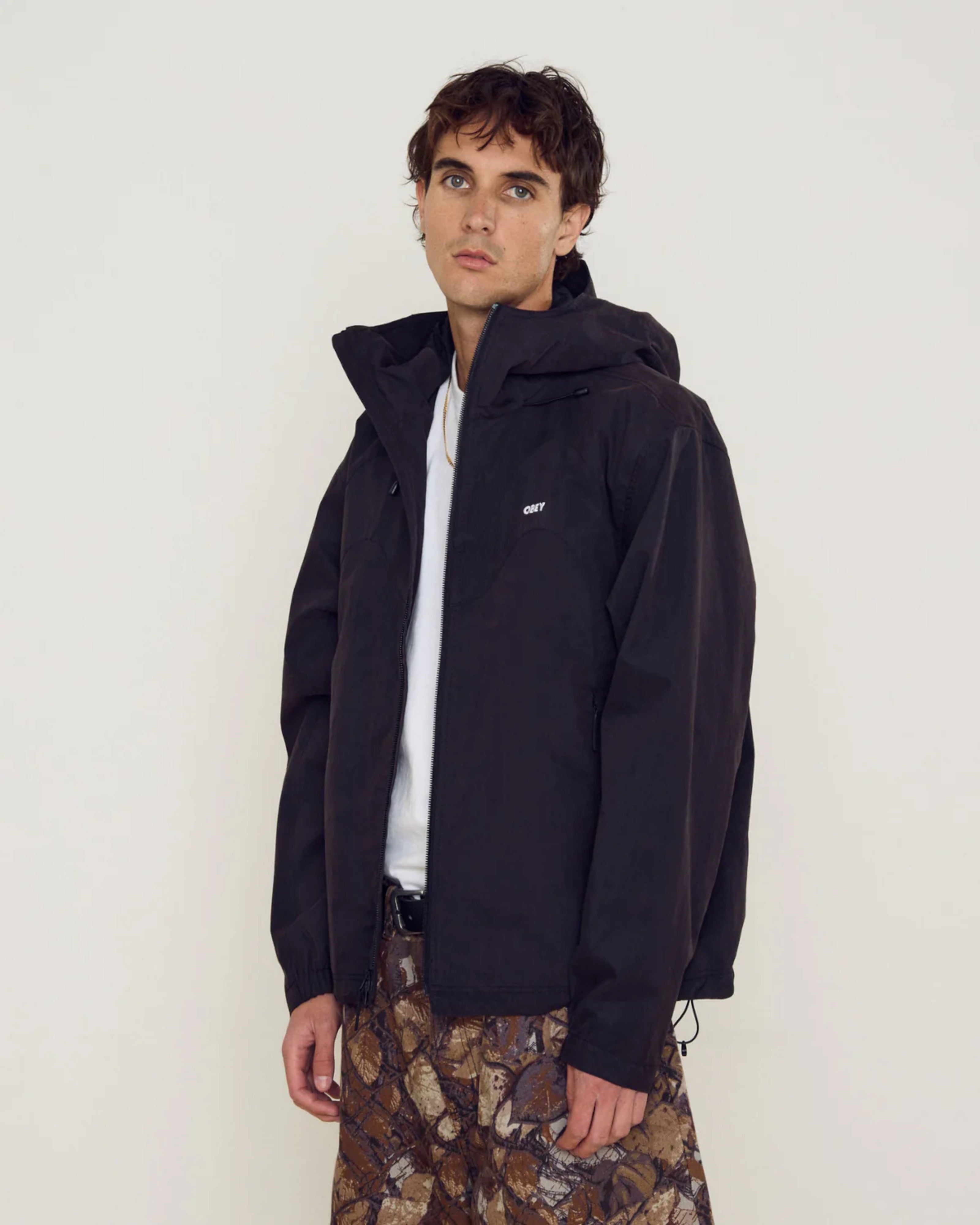 Astrofat Obey Sota Shell Jacket in black, featuring a relaxed fit, adjustable hood, zip pockets, and elasticated cuffs.