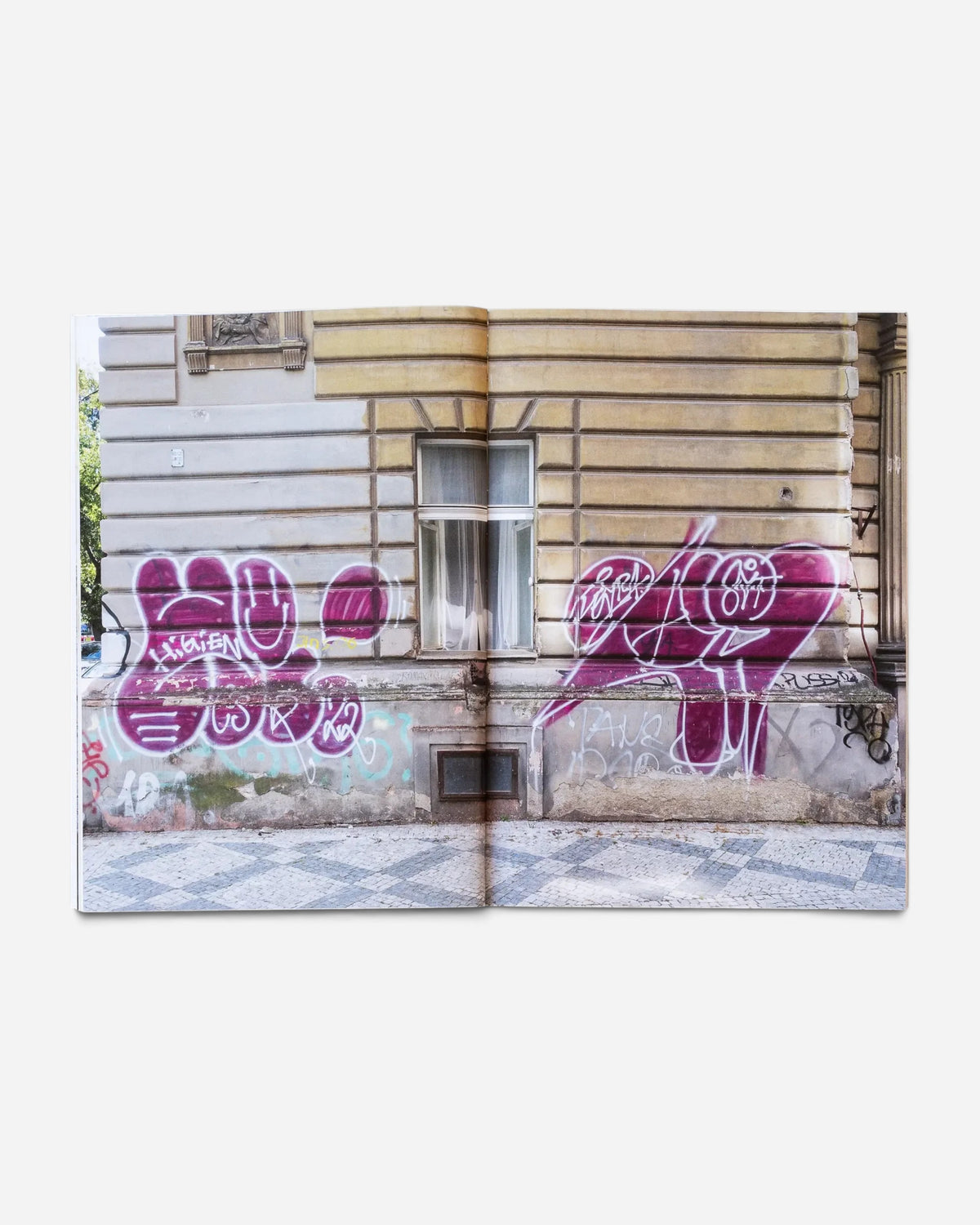 Astrofat zine Praha Tourist Information open to a page showing purple graffiti tags on a historic Prague building wall.