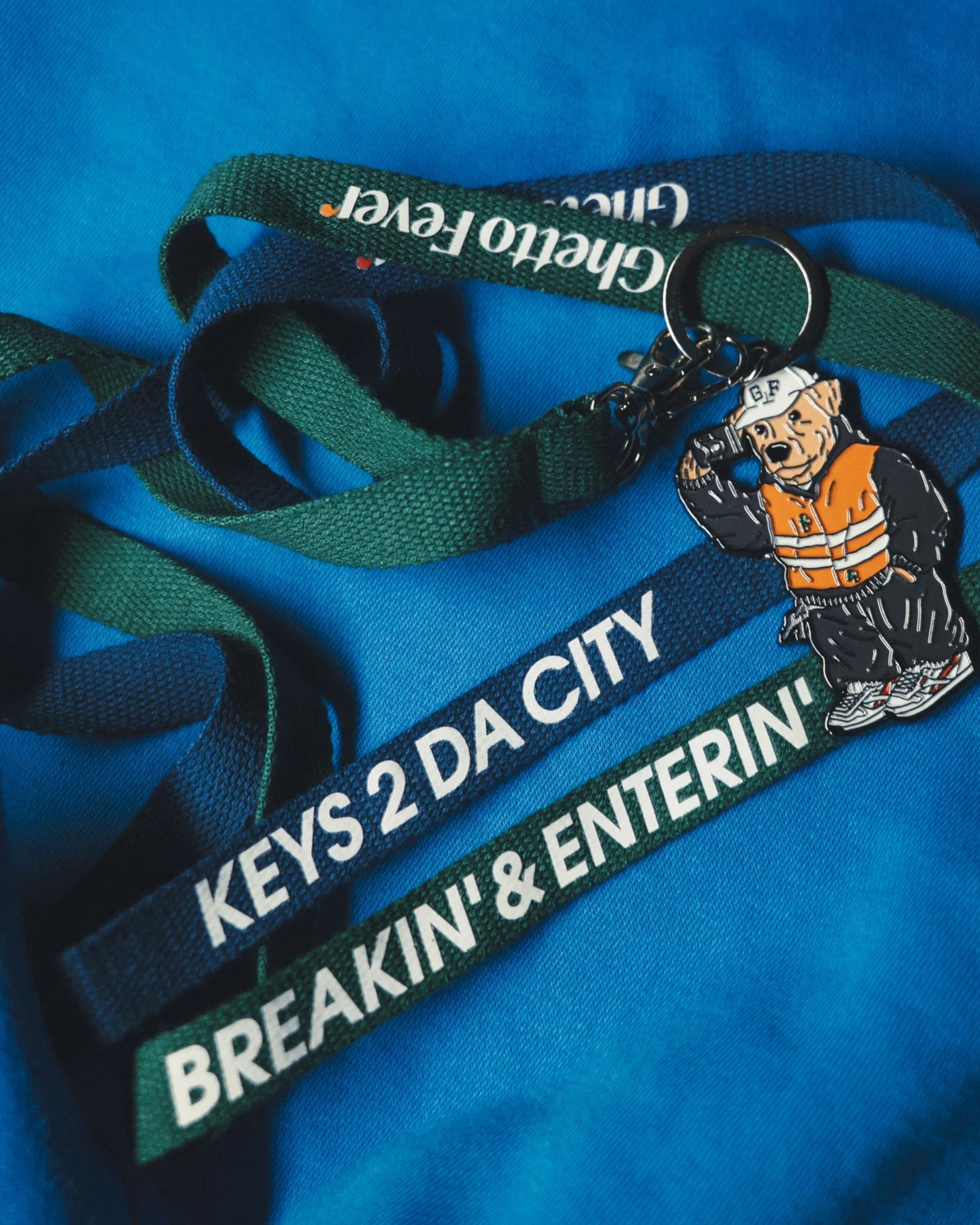 Astrofat Ghetto Fever Underdog rubber keychain with metal ring and green branded lanyard on blue fabric